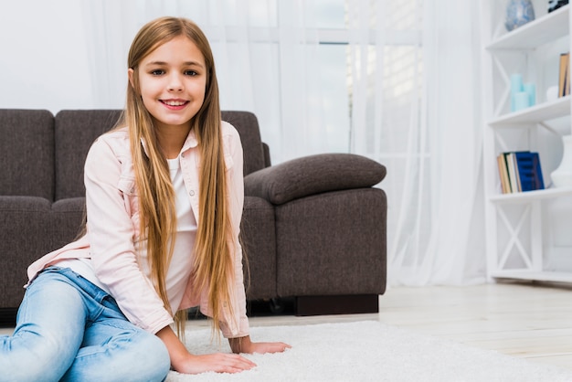 Gratis foto behandel het glimlachen meisjeszitting op wit tapijt kijkend aan camera