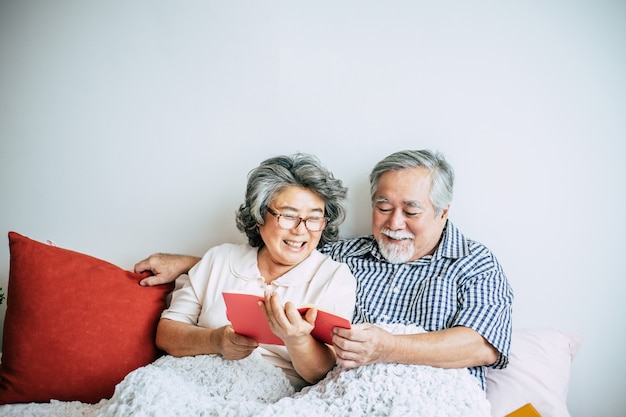 Bejaard Paar dat op het bed ligt en een boek leest