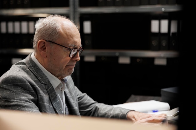 Gratis foto bejaarde boekhoudingszakenman bij het bureau van het dossierkabinet die boekhoudkundige analytische gegevenspapierwerk controleren. administratie senior executive in bedrijfsrepository gevuld met documentmappen