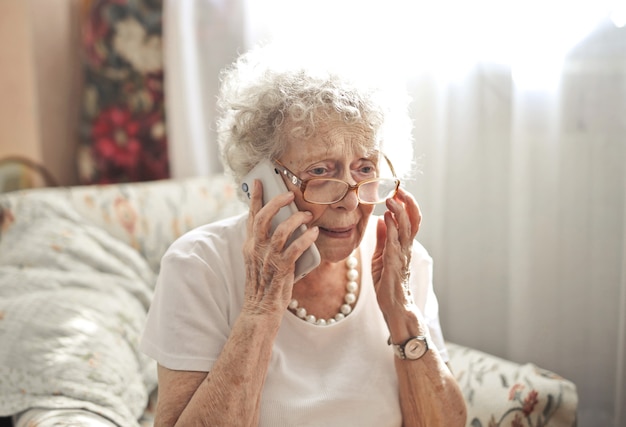 Bejaarde vrouw zittend aan een telefoongesprek met een bezorgde blik op haar gezicht