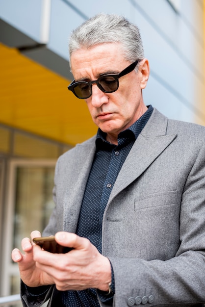 Gratis foto bejaarde zakenman die mobiele telefoon bekijkt