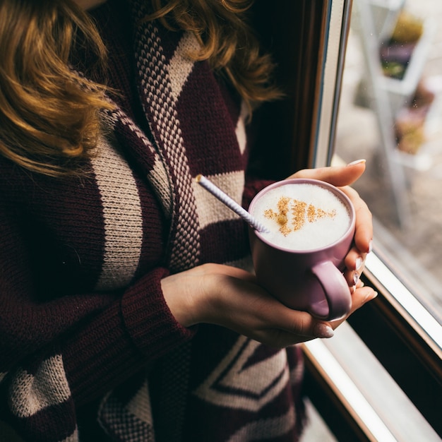 Beker met melk schuim en kerstboom van kaneel in de armen van de vrouw