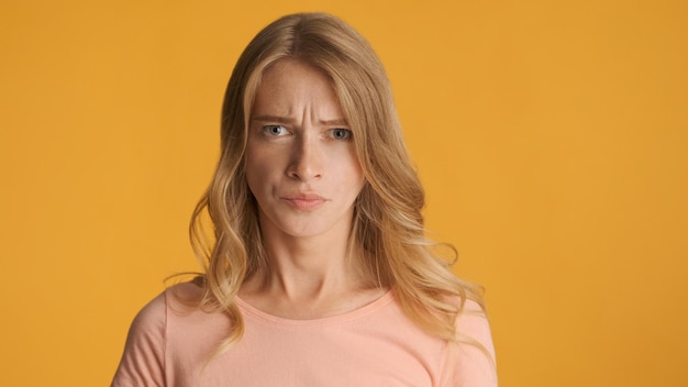 Beledigd blond meisje dat boos in de camera kijkt over kleurrijke achtergrond. Boos uitdrukking