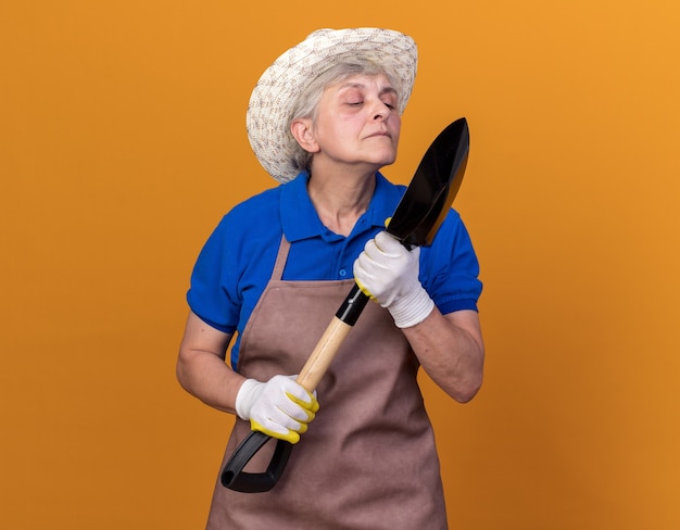 Beledigde oudere vrouwelijke tuinman die een tuinhoed draagt en naar een schop kijkt