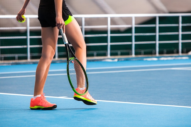 Benen van jong meisje in een gesloten tennisbaan met bal en racket