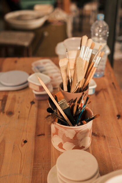 Benodigdheden met verf penselen en gereedschappen in handgemaakte klei houder op houten tafel