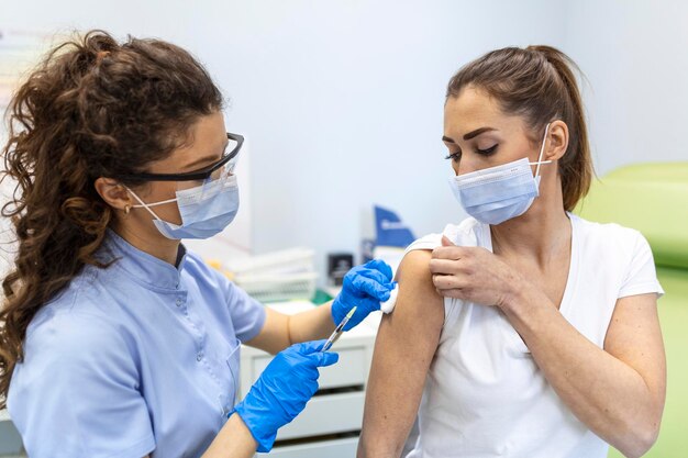 Beoefenaar die vrouwelijke patiënt in kliniek vaccineert Arts die injectie geeft aan vrouw in ziekenhuis Verpleegkundige die spuit vasthoudt en Covid19 of coronavirusvaccin injecteert Injectie covid vaccinconcept