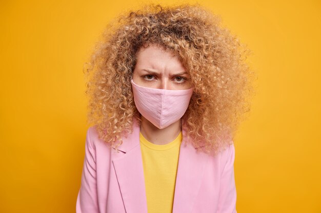 Beperk het risico op verspreiding van virussen. Ontevreden vrouw in formele kleding draagt een beschermend masker om te voorkomen dat het coronavirus een virusvaccin nodig heeft dat over een gele muur is geïsoleerd. Epidemische uitbraak quarantaine