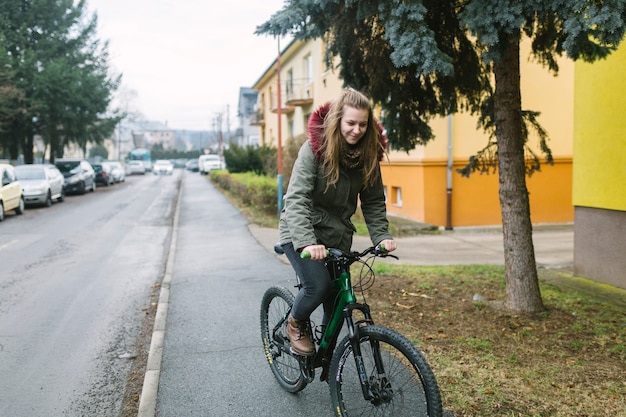 Berijdende fiets van de blonde de jonge vrouw op weg in de stad