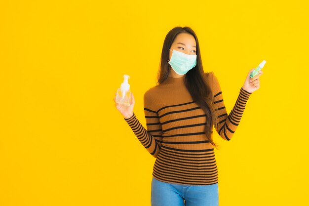 Beschermt de portret mooie jonge Aziatische vrouw met de nevel van de maskeralcohol en gelfles in haar hand voor tegen coronavirus of covid19