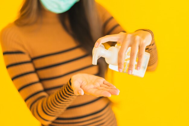 Beschermt de portret mooie jonge Aziatische vrouw met de nevel van de maskeralcohol en gelfles in haar hand voor tegen coronavirus of covid19