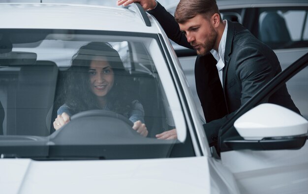 Beschrijf hoe u erover denkt. Vrouwelijke klant en moderne stijlvolle bebaarde zakenman in de auto-salon