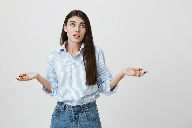 Besluiteloze schattige vrouw die haar schouders ophaalt, haar handen opzij geen idee heeft