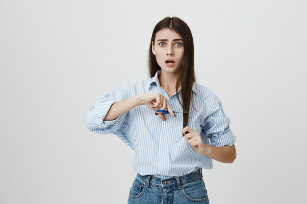 Besluiteloze vrouw die gespleten haarpunten snijdt met een schaar, kijk bezorgd