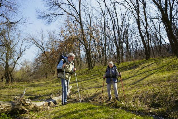 Beste momenten samen. Leeftijd familie paar man en vrouw in toeristische outfit wandelen op groen gazon in zonnige dag in de buurt van kreek. Concept van toerisme, gezonde levensstijl, ontspanning en saamhorigheid.