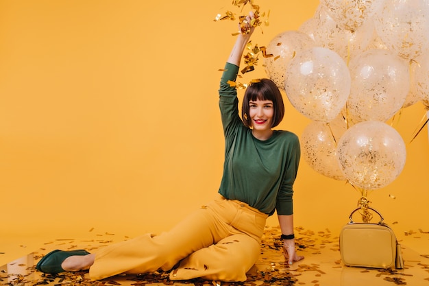 Gratis foto betoverend meisje met kort haar dat confetti weggooit. portret van vrolijke jonge vrouw gek rond in haar verjaardag.