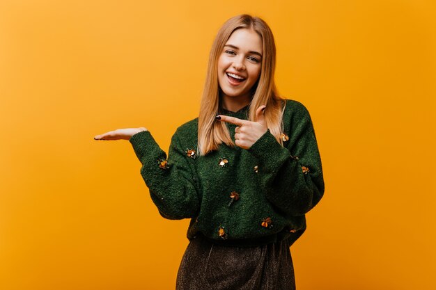 Betoverende blinde vrouw in trendy gebreide trui die geluk uitdrukt. Binnenportret van charmante Europese vrouw die zich op sinaasappel bevindt.