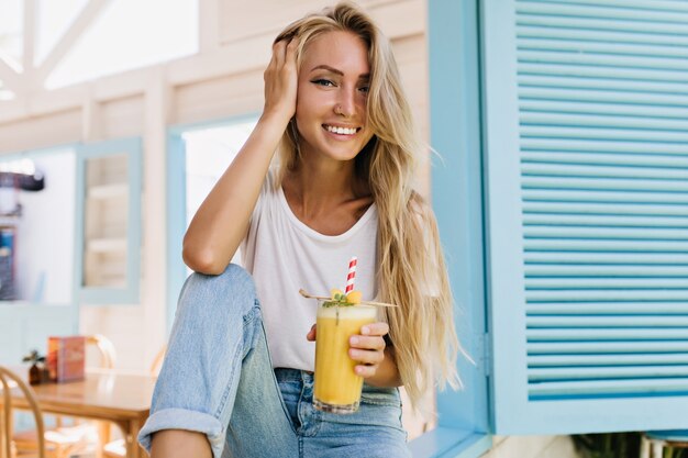 Betoverende langharige dame die met plezier cocktail drinkt. Foto van het positieve Europese glas van de vrouwenholding koude drank.