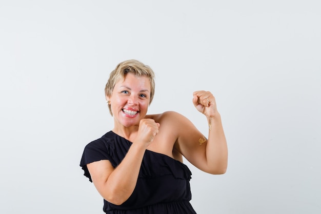 Betoverende vrouw die winnaargebaar in zwarte blouse toont en energiek kijkt