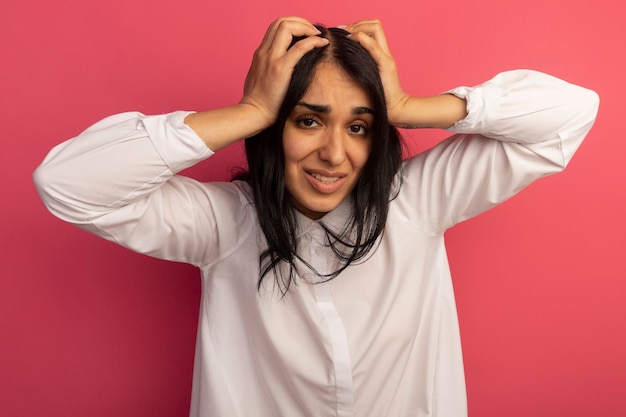 Betrokken jong mooi meisje met een witte t-shirt greep hoofd geïsoleerd op roze