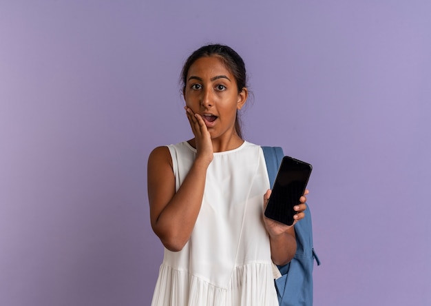 Betrokken jong schoolmeisje die de telefoon van de rugzakholding dragen en hand op wang zetten