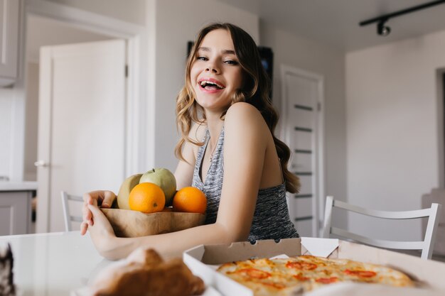 Bevallige vrouw die met elegant kapsel sinaasappel eet. Binnenfoto van prachtig Kaukasisch meisje dat van fruit geniet.