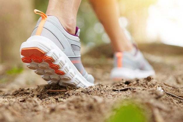 Bevriezen actie close-up van jonge vrouw lopen of rennen op pad in bos of park in zomer natuur buitenshuis. Atletisch meisje dat sportschoenen draagt, die op voetpad uitoefent.