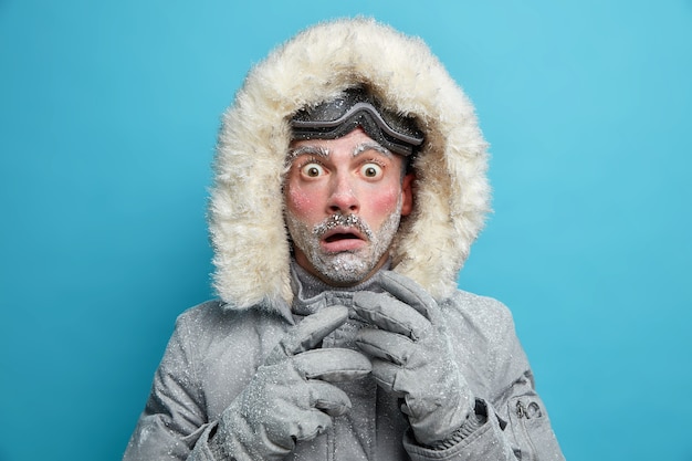 Gratis foto bevroren mannelijke ontdekkingsreiziger heeft rood gezicht bedekt met vorst staart zeer geschokt verrast door zeer lage temperatuur draagt warme jas en handschoenen loopt buiten tijdens sneeuwstorm koud weer