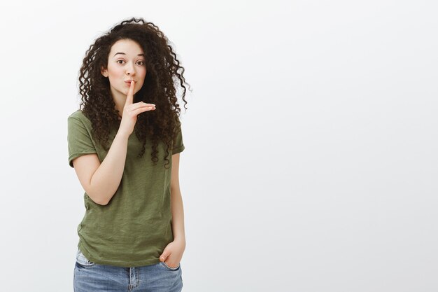 Bewaar ons kleine geheimpje. Portret van speelse intrigerende aantrekkelijke vrouw met krullend haar