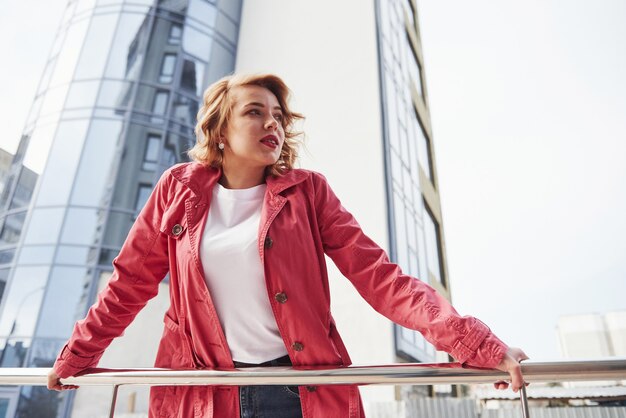 Bewolkte lucht. Volwassen mooie vrouw in warme rode jas wandelt in het weekend door de stad