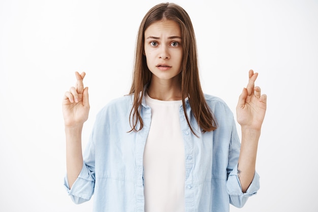 Gratis foto bezorgd en ongerust charmante vrouwelijke brunette met medium kapsel fronsend op zoek nerveus vingers kruisen voor geluk wensen doen of bidden wachten op belangrijke dingen gebeuren