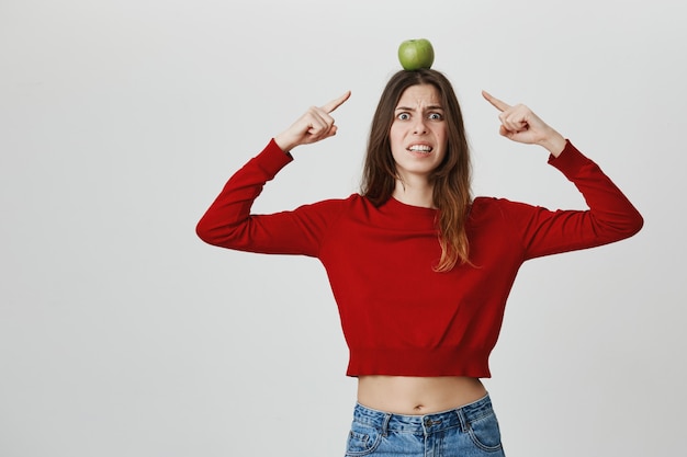 Bezorgd grijnzende mooie vrouw die op groene appeldoel op haar hoofd richt