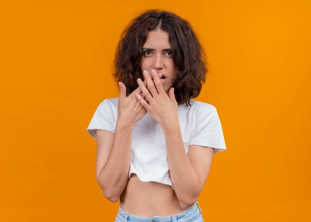 Bezorgde jonge mooie vrouw die handen op mond op geïsoleerde oranje muur met exemplaarruimte zet