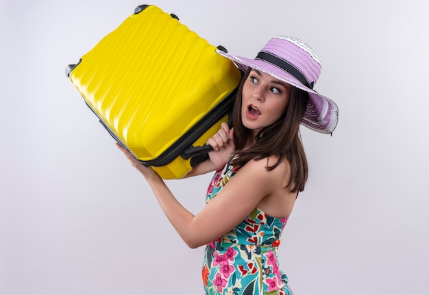 Bezorgde jonge reizigersvrouw die de koffer van de hoedenholding op geïsoleerde witte muur dragen