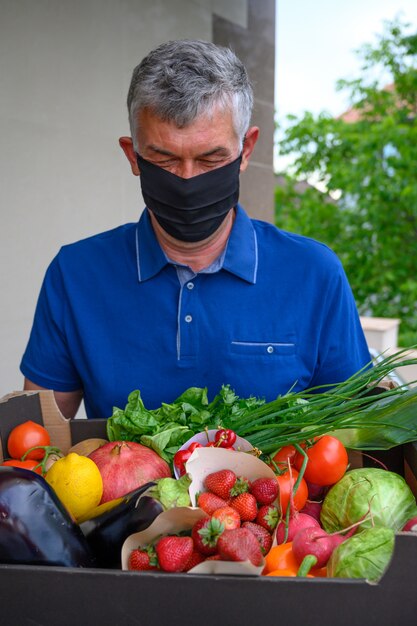 Bezorger die een gezichtsmasker draagt en een doos met groenten houdt