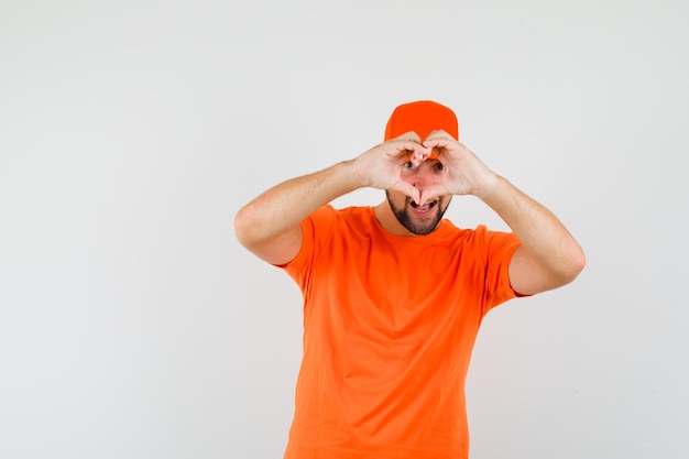 Bezorger die hartgebaar toont in oranje t-shirt, pet en er blij uitziet. vooraanzicht.