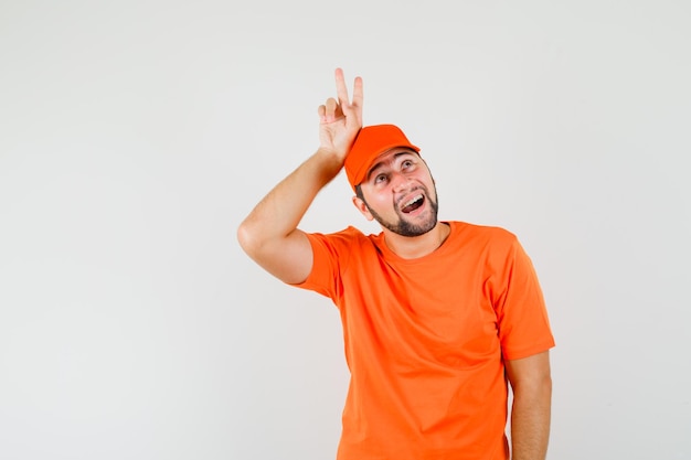 Bezorger die v-teken boven het hoofd toont in oranje t-shirt, pet en er grappig uitziet. vooraanzicht.