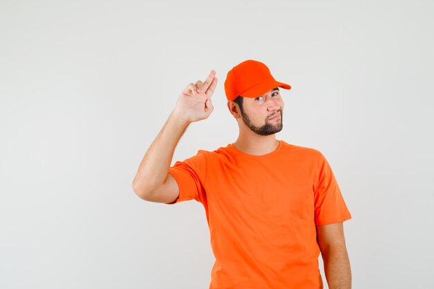 Bezorger gebaart met twee vingers in oranje t-shirt, pet en ziet er zelfverzekerd uit. vooraanzicht.