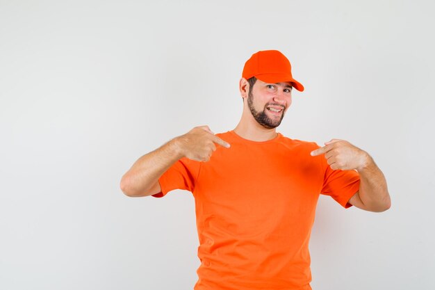 Bezorger in oranje t-shirt, pet die naar zichzelf wijst en er trots uitziet, vooraanzicht.