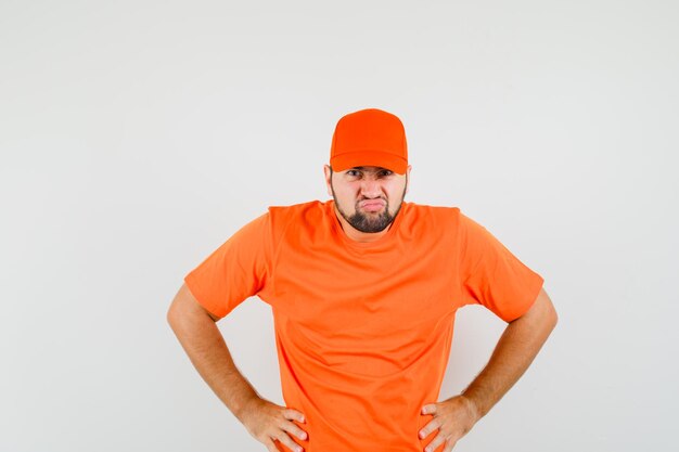 Bezorger in oranje t-shirt, pet hand in hand op taille en koppig kijkend, vooraanzicht.