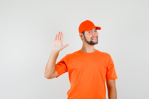 Bezorger in oranje t-shirt, pet met palm en vrolijk, vooraanzicht.