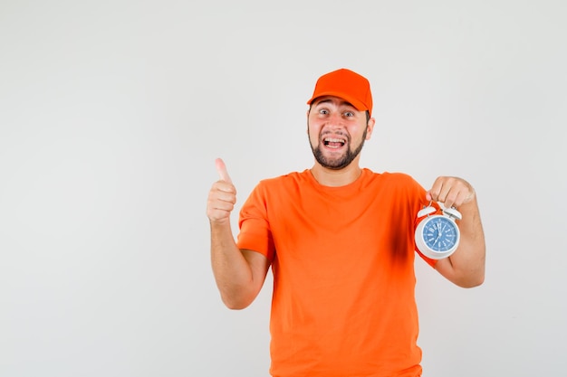 Bezorger in oranje t-shirt, pet met wekker met duim omhoog en ziet er gelukkig uit, vooraanzicht.