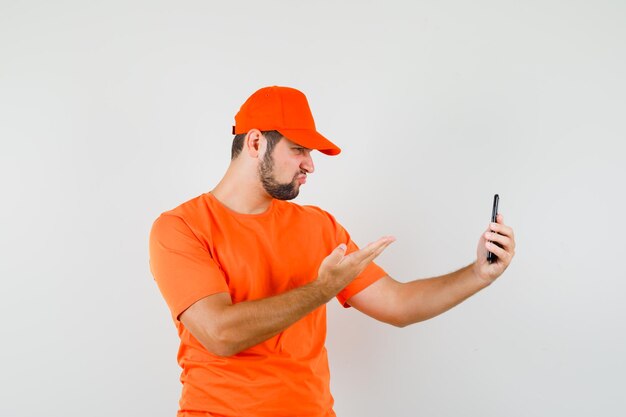 Bezorger in oranje t-shirt, pet pratend op videogesprek en boos kijkend, vooraanzicht.