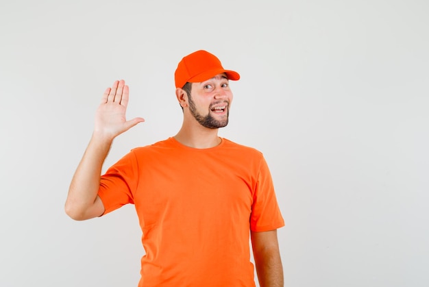 Bezorger in oranje t-shirt, pet zwaaiend met de hand om hallo of vaarwel te zeggen en er vrolijk uit te zien, vooraanzicht.