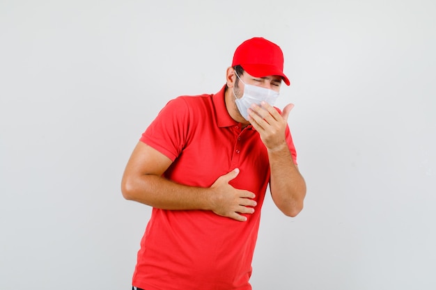 Bezorger in rood t-shirt, pet, masker dat aan hoest lijdt en er ziek uitziet