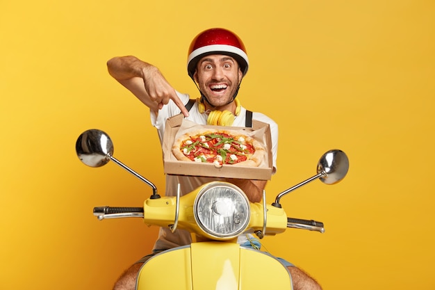 Gratis foto bezorger met helm gele scooter rijden terwijl pizzadoos vasthoudt