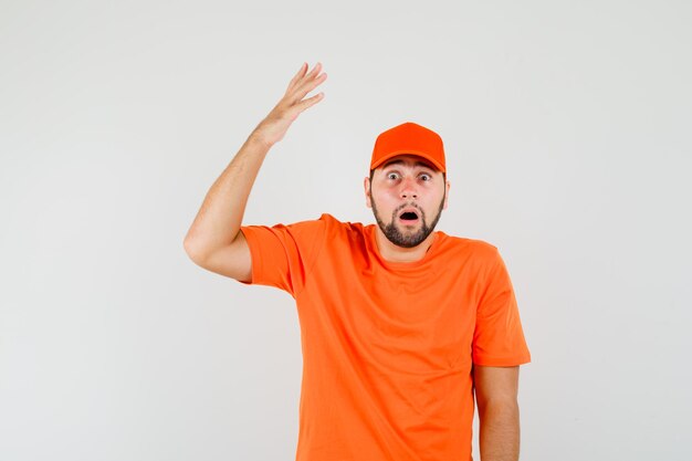 Bezorger steekt hand op in oranje t-shirt, pet en kijkt geschokt. vooraanzicht.