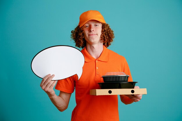 Bezorger werknemer in oranje pet leeg t-shirt uniform met lege tekstballon en voedselcontainers kijkend naar camera met zelfverzekerde uitdrukking glimlachend staande over blauwe achtergrond