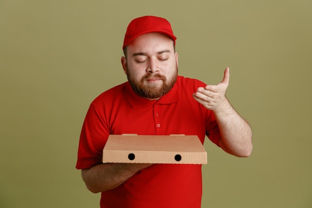 Bezorger werknemer in rode dop leeg t-shirt uniform met pizzadoos staande over groene achtergrond