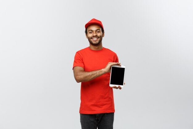 Bezorgingsconcept - Portret van knappe Afro-Amerikaanse leveringsman of koerier met een tablet op u om de bestelling te controleren. Geïsoleerd op grijze studio achtergrond. Ruimte kopiëren.